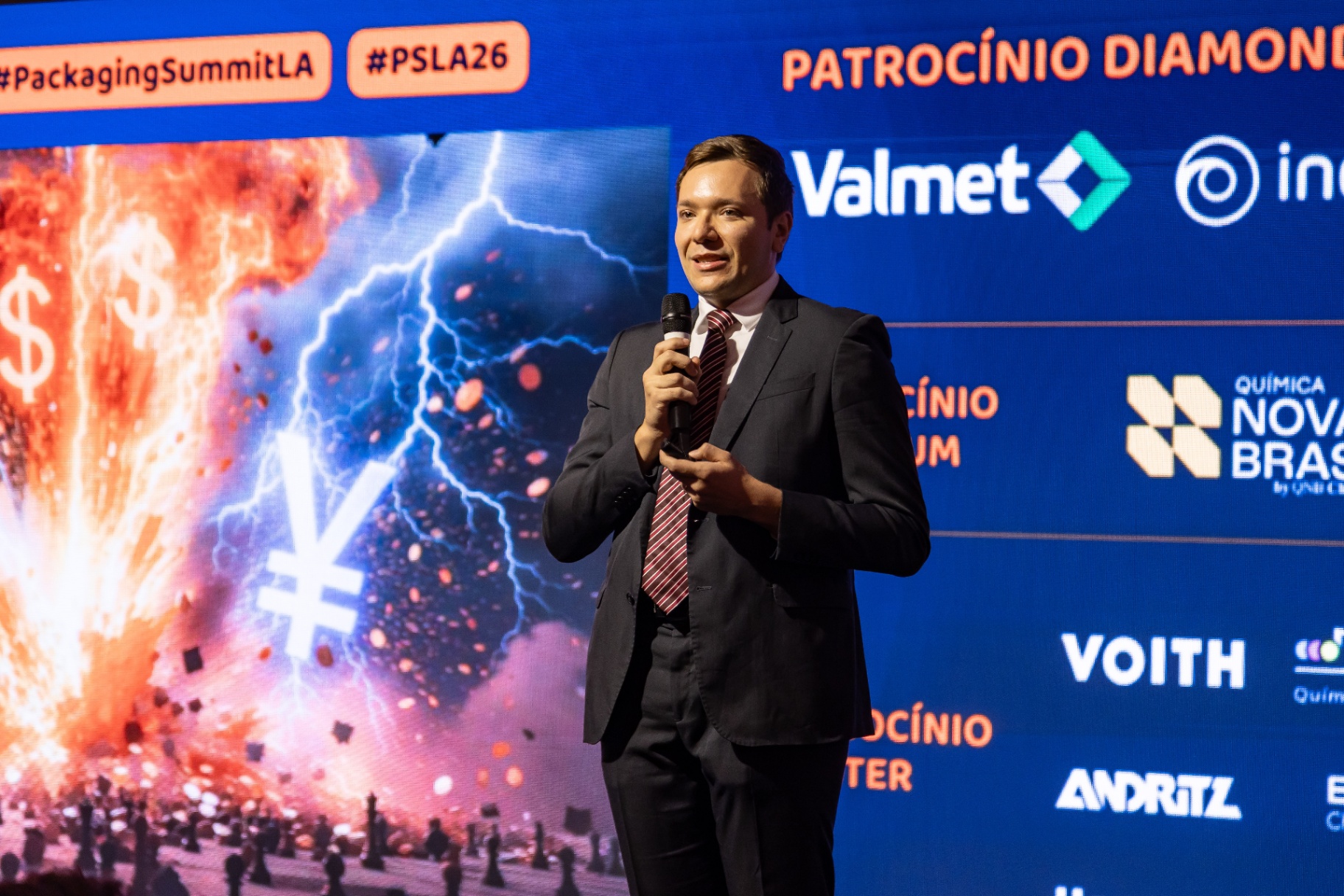Palestrante no palco principal com patrocinadores ao fundo